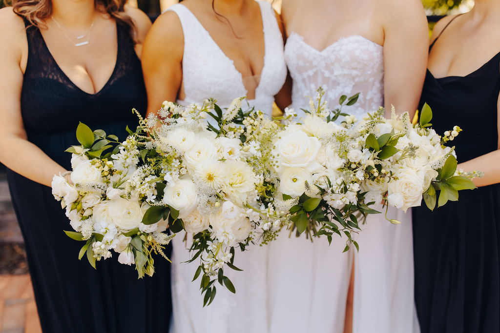 Four individuals in a wedding party holding elaborate bouquets with white flowers and greenery.
