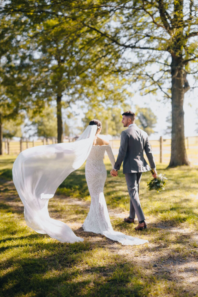 A wedding couple holding hands and walking in a wooded area. 