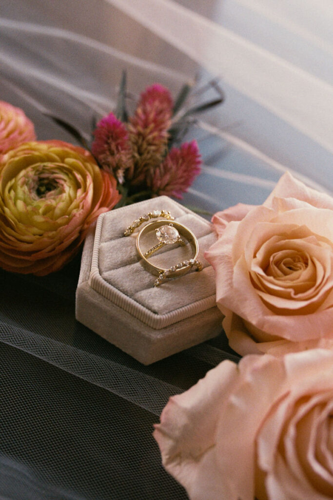 Close-up of an elegant wedding ring and band set in a soft velvet box, surrounded by vibrant flowers