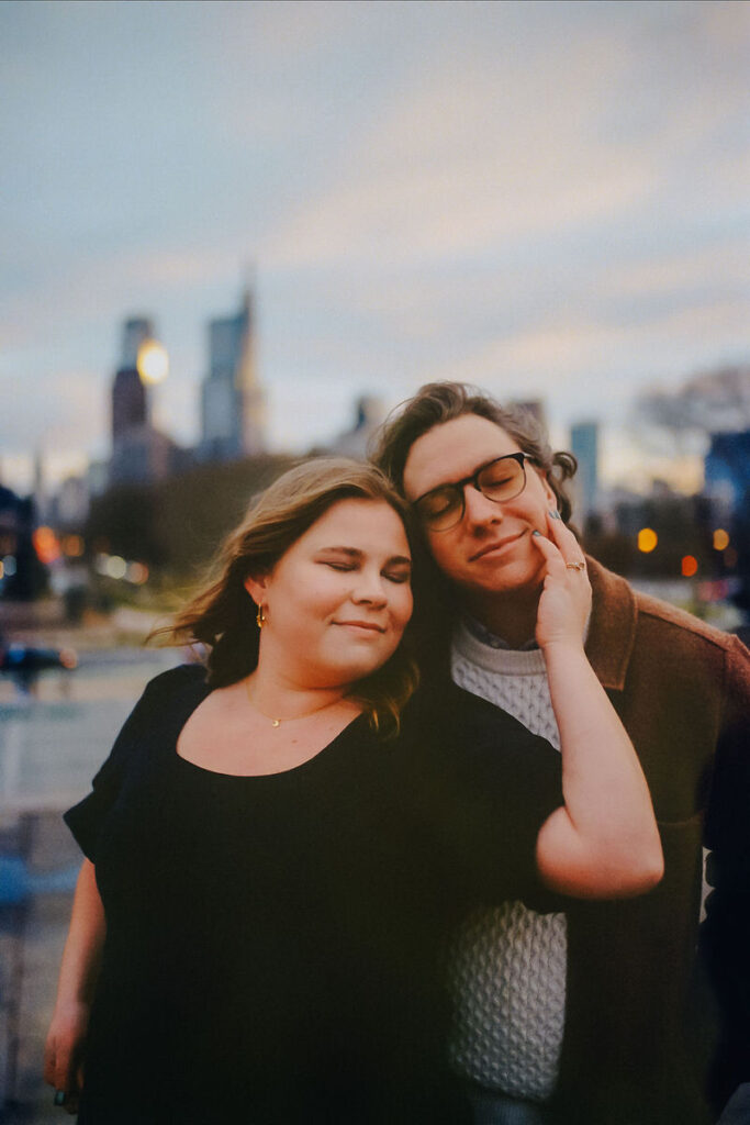 A romantic film photograph of a couple embracing in front of a cityscape at twilight