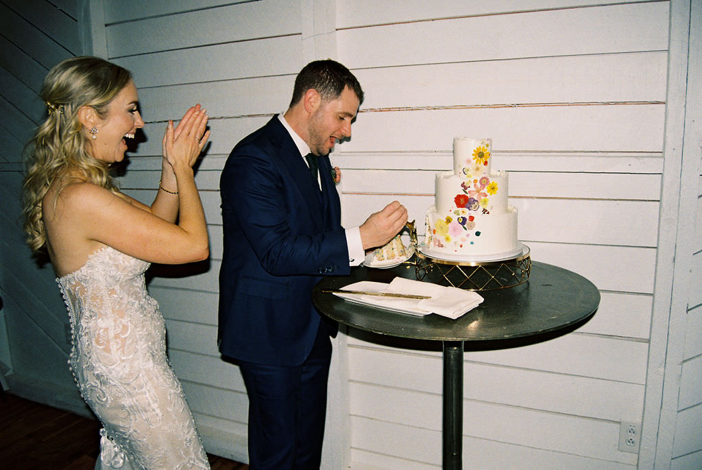 A wedding couple enthusiastically preparing to cut a colorful, floral-painted wedding cake
