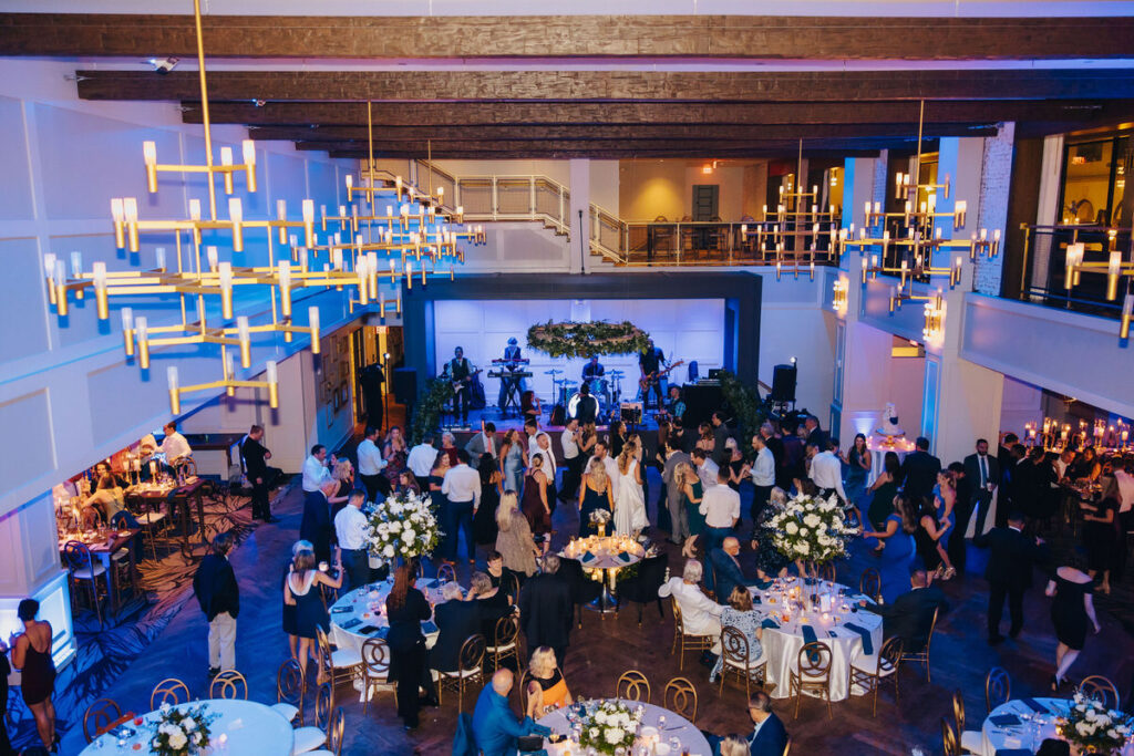 An overhead shot of a wedding reception in a large hall with chandeliers, showing guests dancing and enjoying a live band performance.