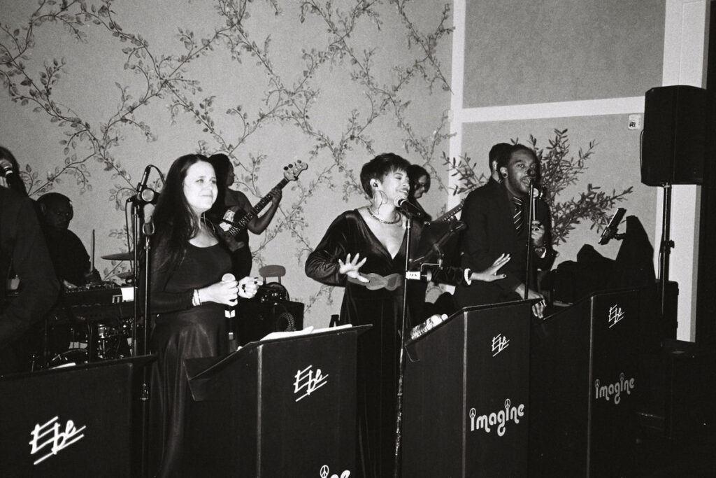 A black and white photo of a live band with various musicians, including a violinist and singers, performing at a wedding.