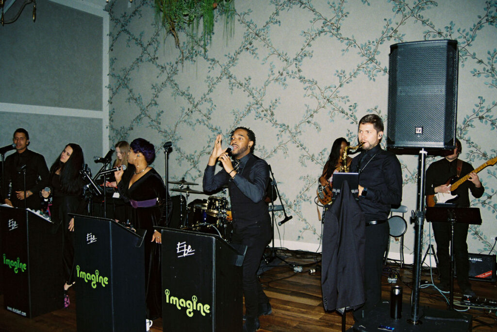A lively band performing at a wedding reception, with a focus on a male singer and instrumentalists engaging with the audience.
