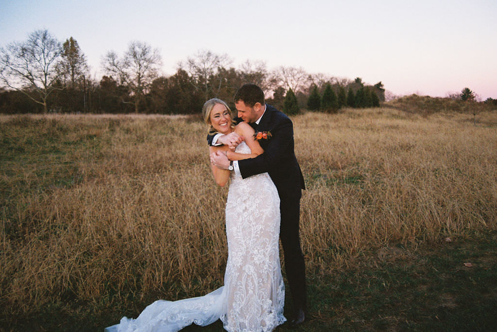 A couple hugging and smiling while standing in a field after their wedding. 