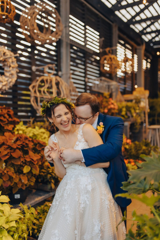A couple sharing a dance and a laugh amidst lush greenery and warm ambient lighting, creating a cozy and intimate moment during their wedding celebration.