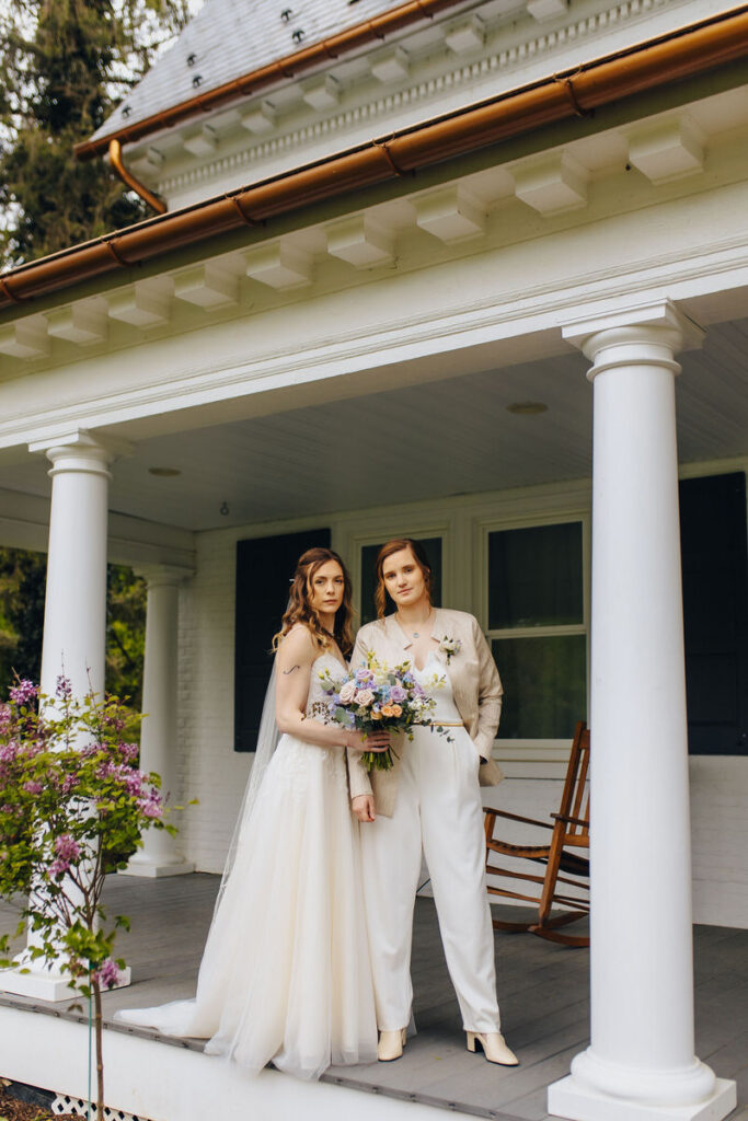 Two brides standing on a patio while one holds a bouquet of flowers. 