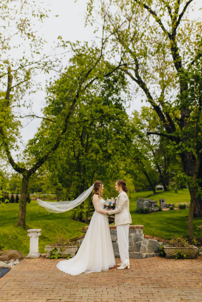 Two brides standing close together on a small brick patio. 
