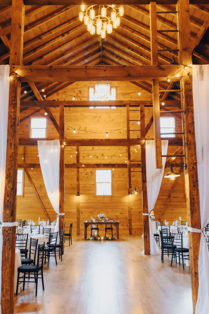 Reception tables set up in a large wooden lodge with string lights overhead. 