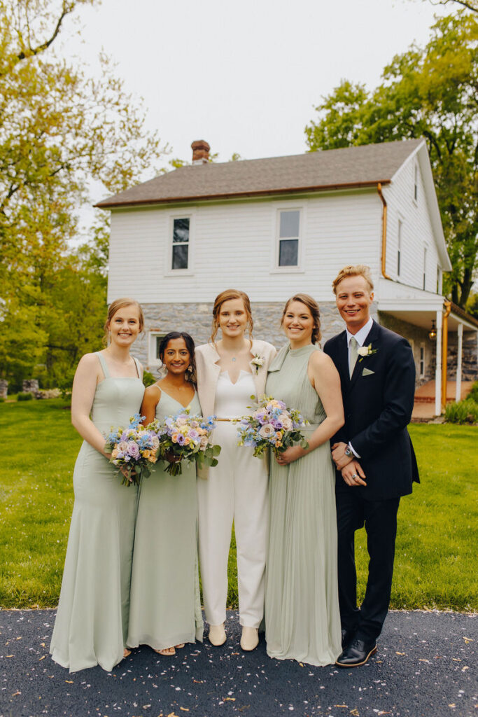A bride standing with her wedding party as they all smile. 
