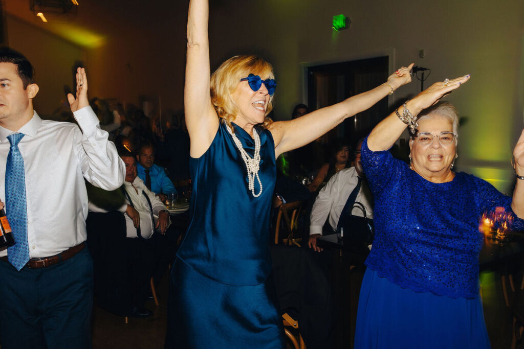 Energetic wedding guests dancing and celebrating at a reception, with colorful lights