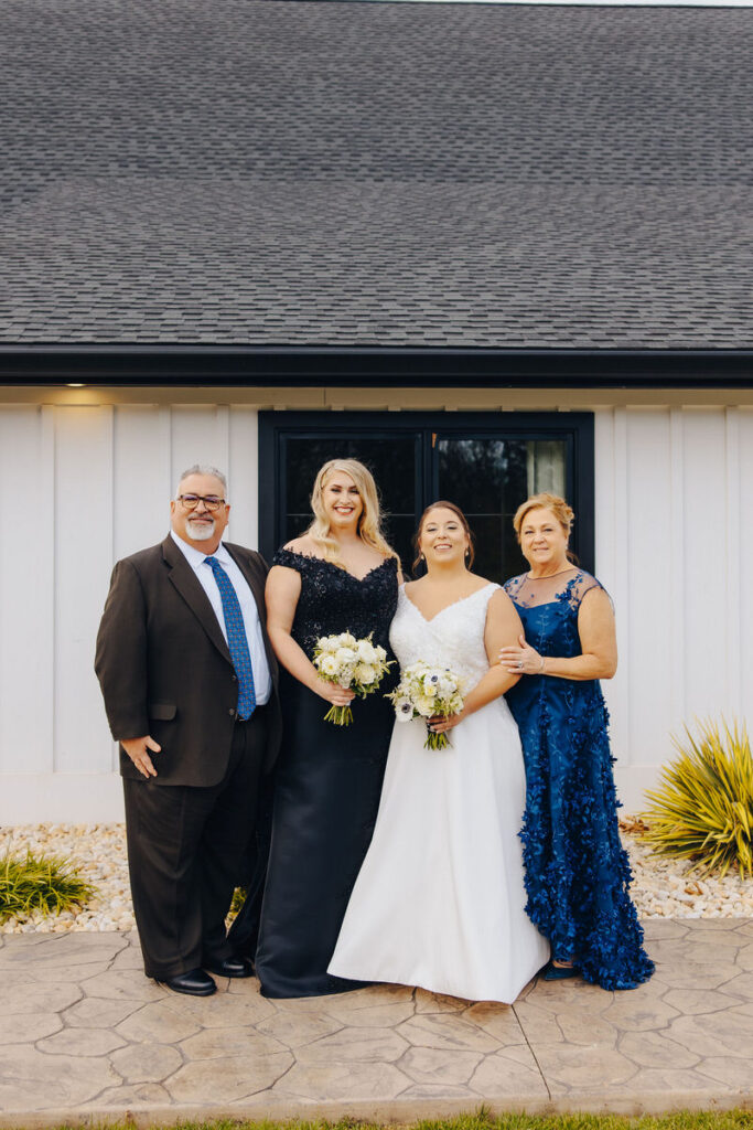 Two brides smiling with a man and a woman on either side of them. 
