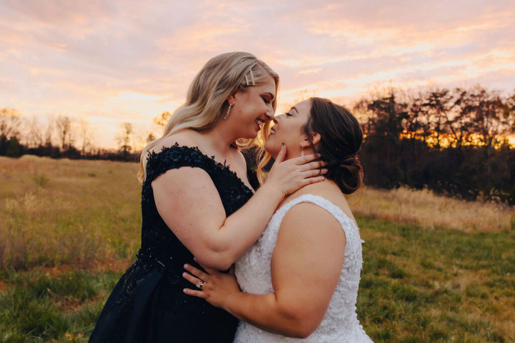 A tender moment between two brides sharing a kiss, set against a stunning golden hour sky