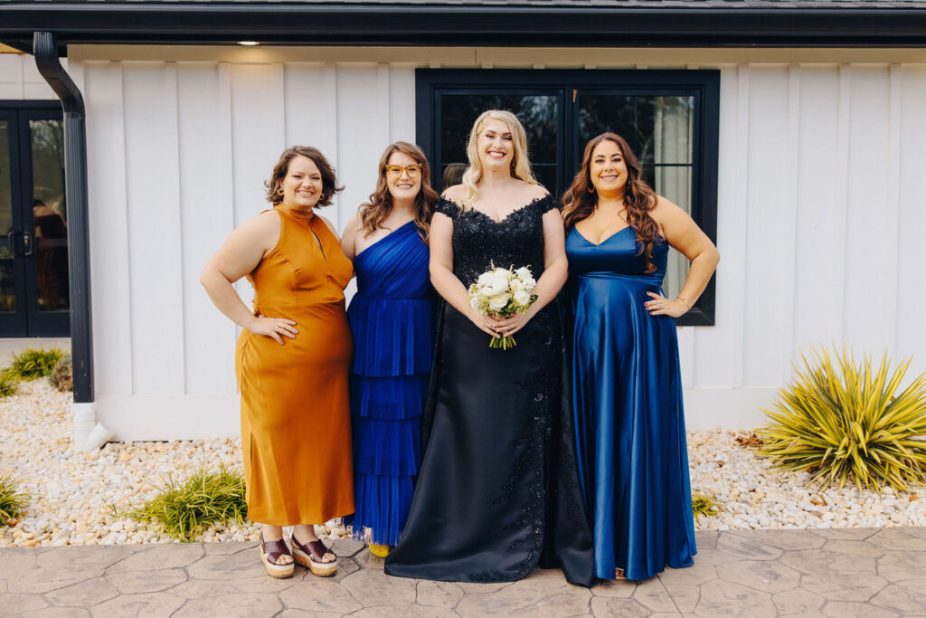 A group of bridesmaids in vibrant dresses pose confidently with the bride outside the wedding venue