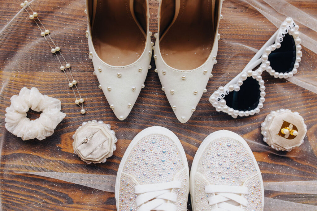 Wedding shoes, rings, jewelry, and sunglasses laid on top of a veil. 