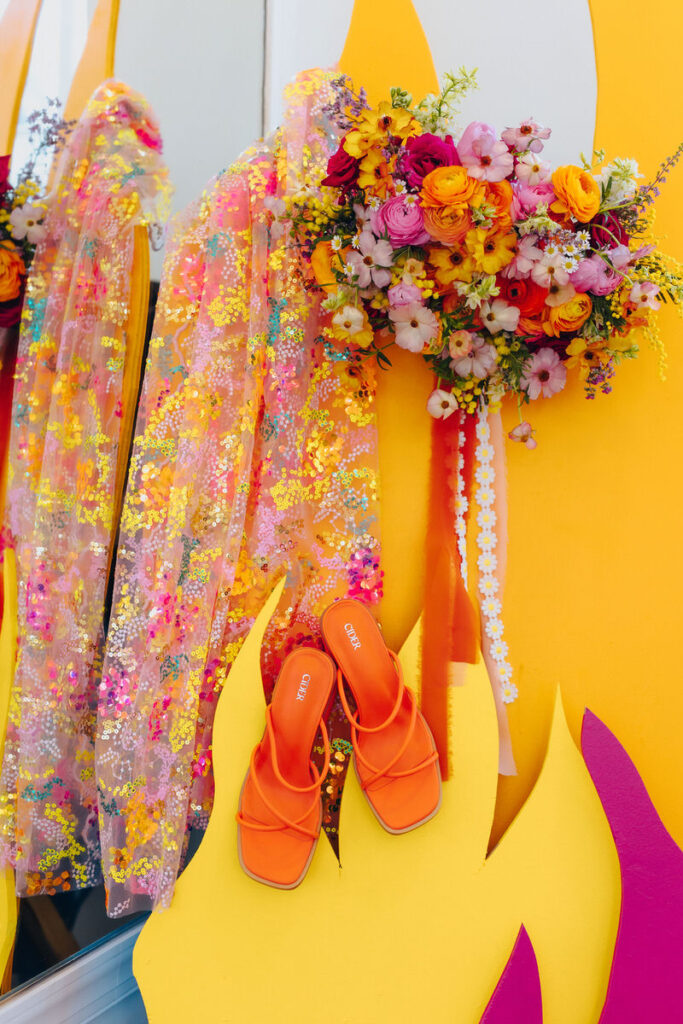 Bright heels and colorful veil hanging next to a bouquet of flowers. 