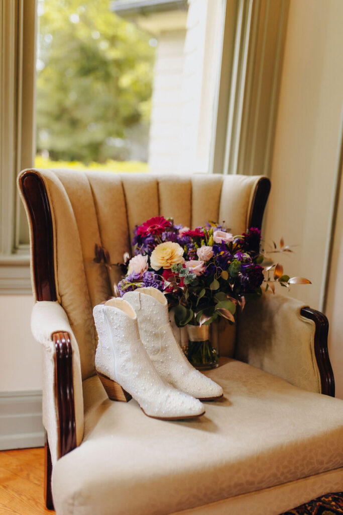 White boots on a chair next to a bouquet of flowers.