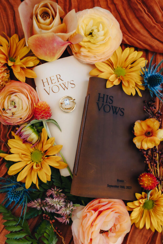 His and her vow books with rings on top and flowers surrounding them. 