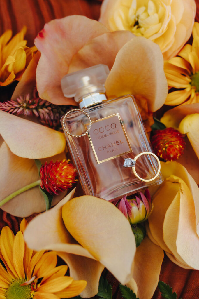 An engagement and wedding band on top of a bottle of perfume surrounded by flower petals. 