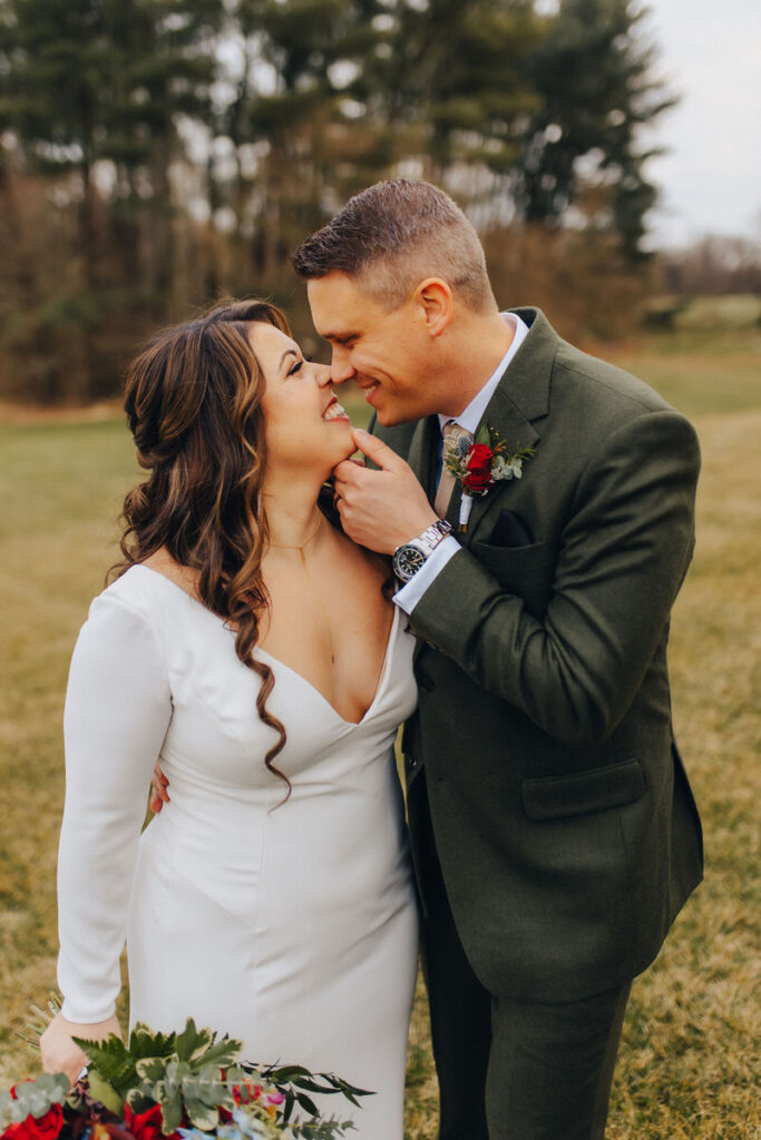 A wedding couple smiling as they lean in for a kiss. 
