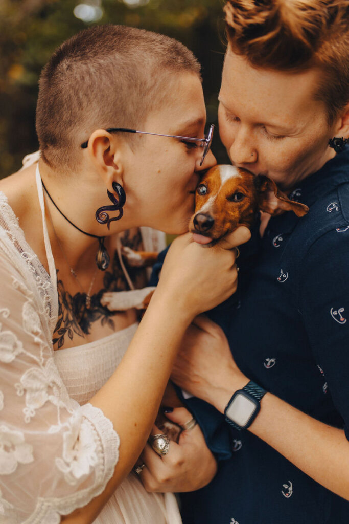  A couple holding a dog between them both kissing it's head. 
