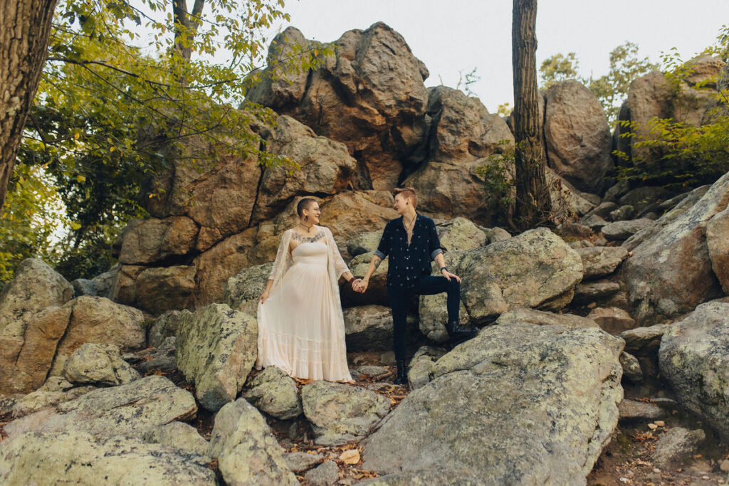 A couple holding hands and standing in a rocky area. 
