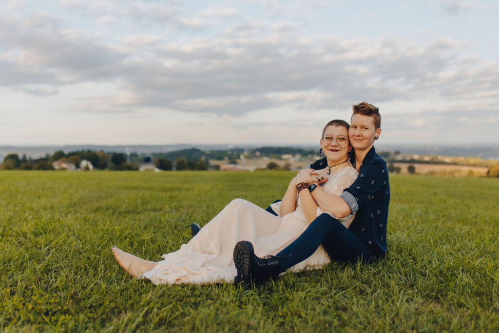 A couple sitting together in a field with their arms around each other. 