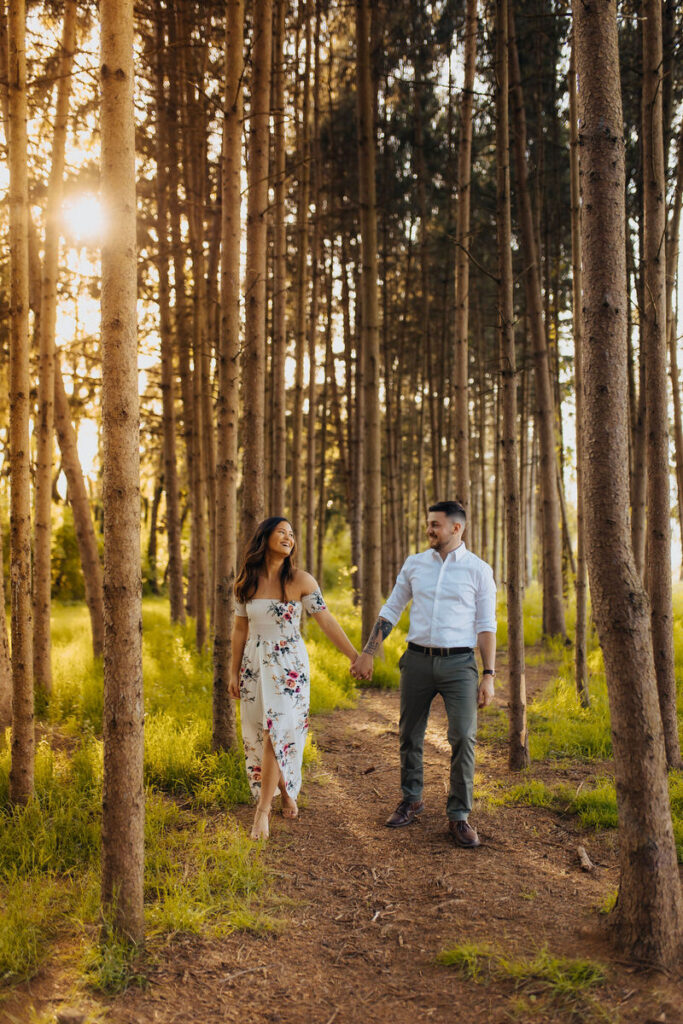 A couple holding hands and walking through a patch of tall skinny trees 