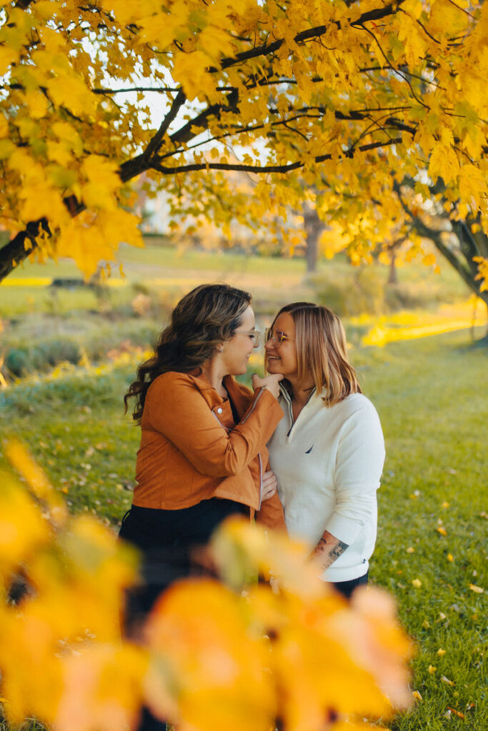A couple about to kiss under a fall colored tree. 