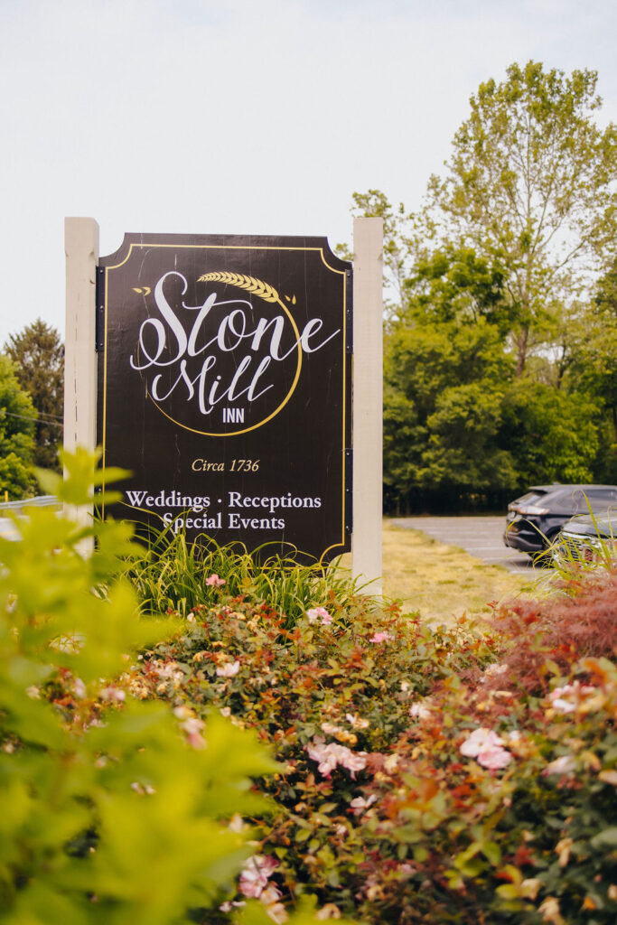 An elegant wooden sign reading "Stone Mill Inn" surrounded by lush plants, indicating the venue specializes in weddings, receptions, and special events.
