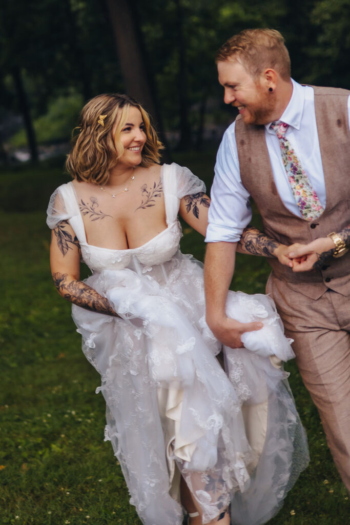 A couple holding hands and walking together while one holds the bottom of the other's wedding dress