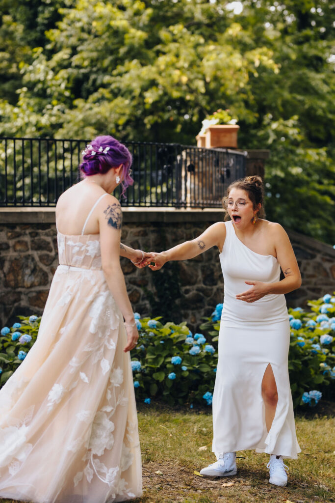 A couple during their first look as they hold hands and one has a shocked look on their face 