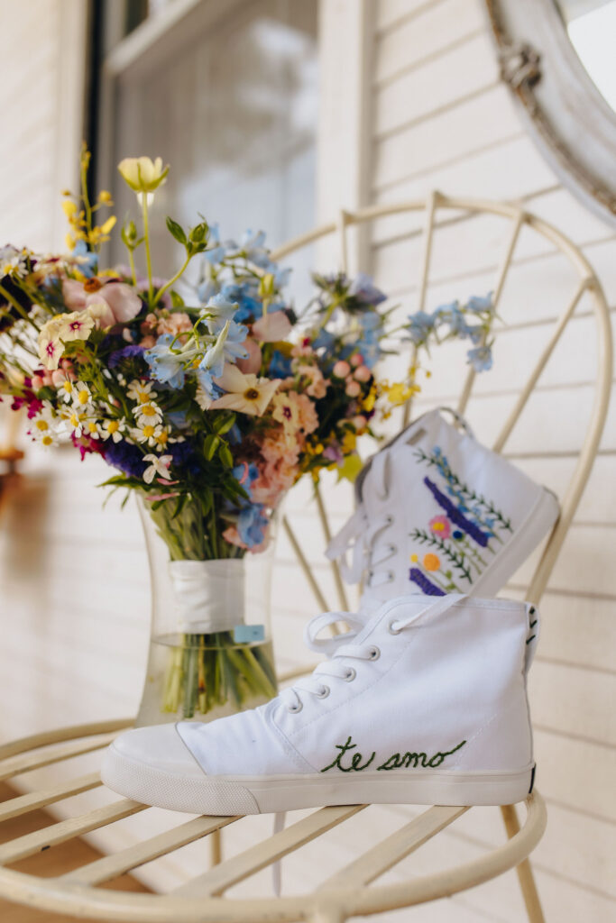 A pair of custom converse next to a bouquet of flowers with flowers stitched on one and "te amo" stitched on another. 