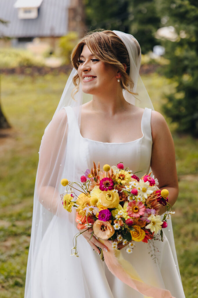 A person in a wedding dress holding a bright bouquet of flowers and smiling. 