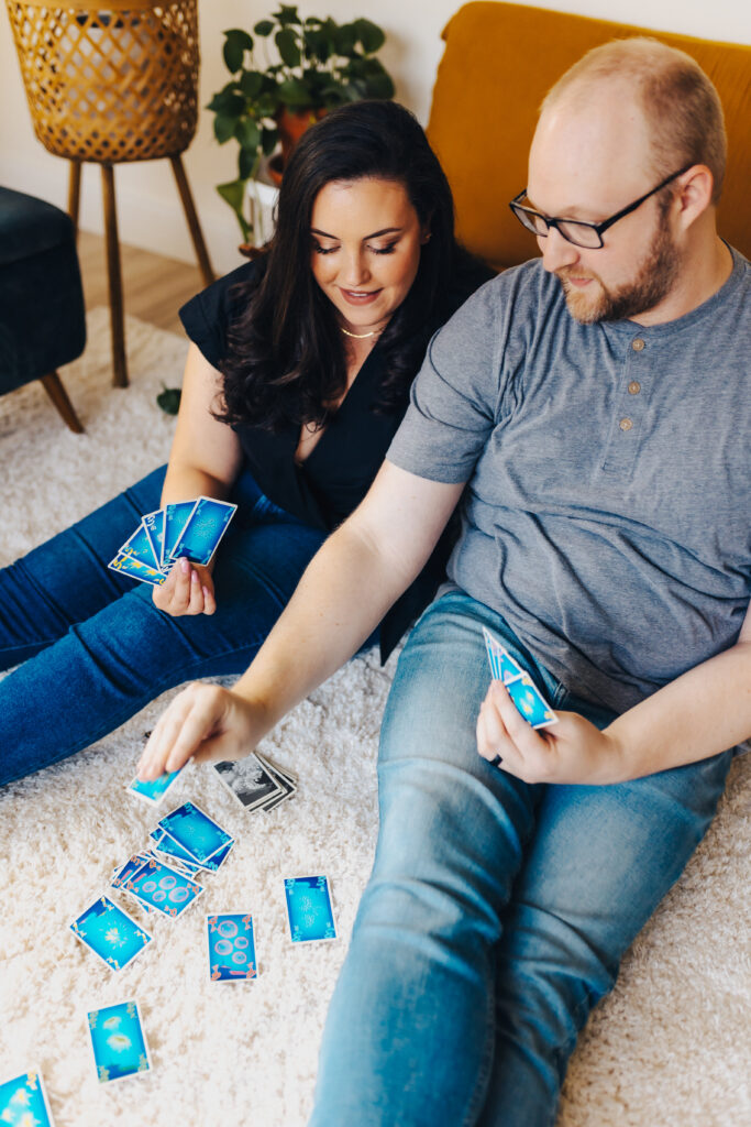 An engaged couple sitting on the floor playing with a blue deck of cards