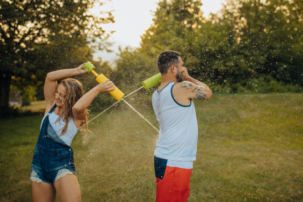 A couple spraying each other with water guns over their shoulders