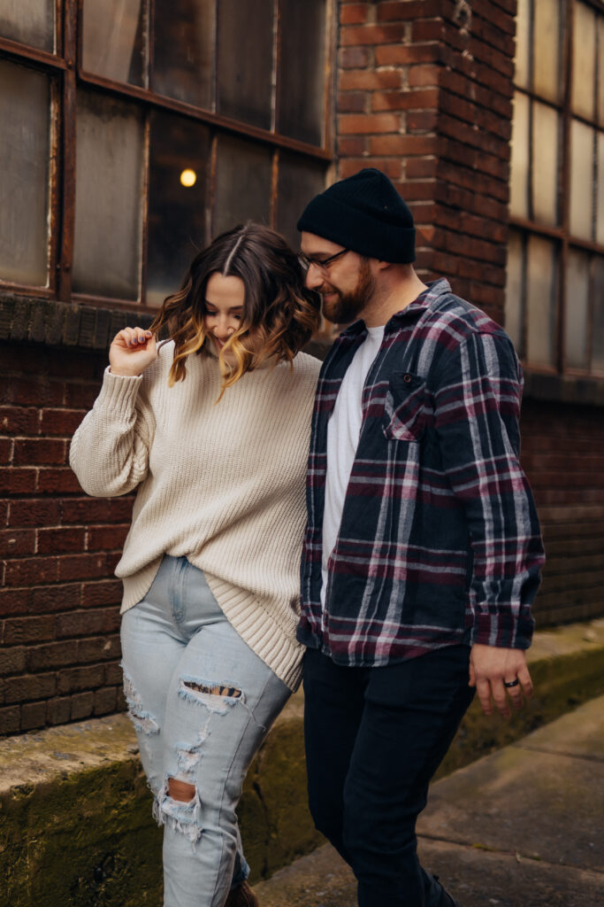 An engaged couple walking down a street with a brick building in the background