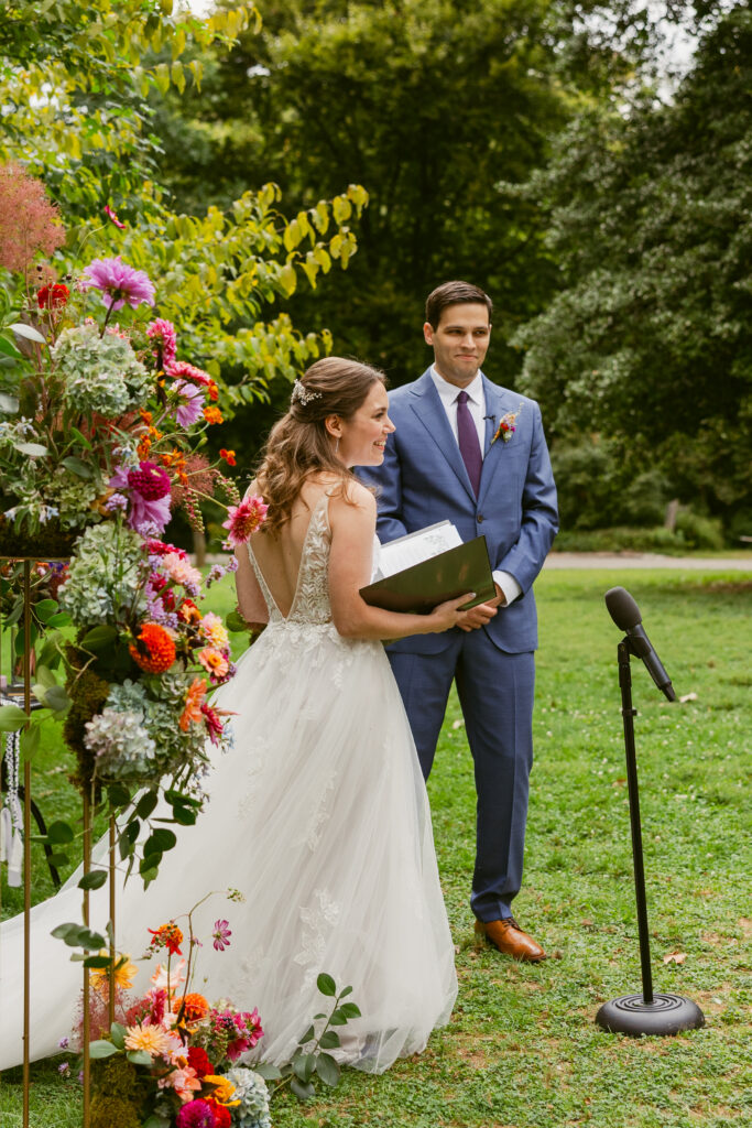 A bride and grooming smiling at their guests as she looks up from reading her vows