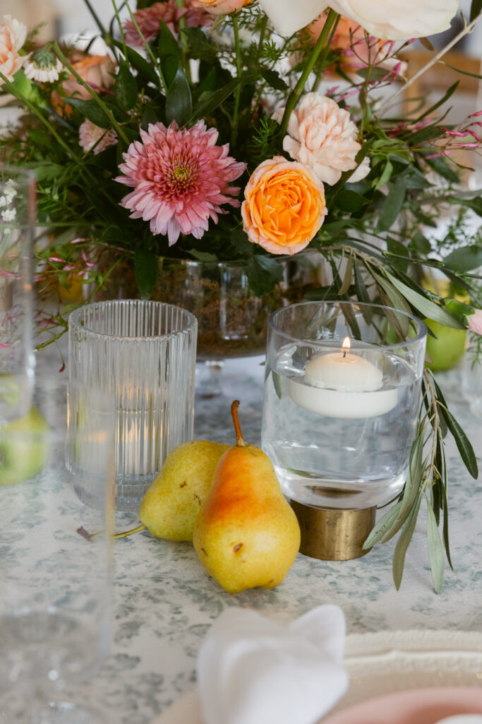 A close-up of a wedding table arrangement of flowers, candles, and pears
