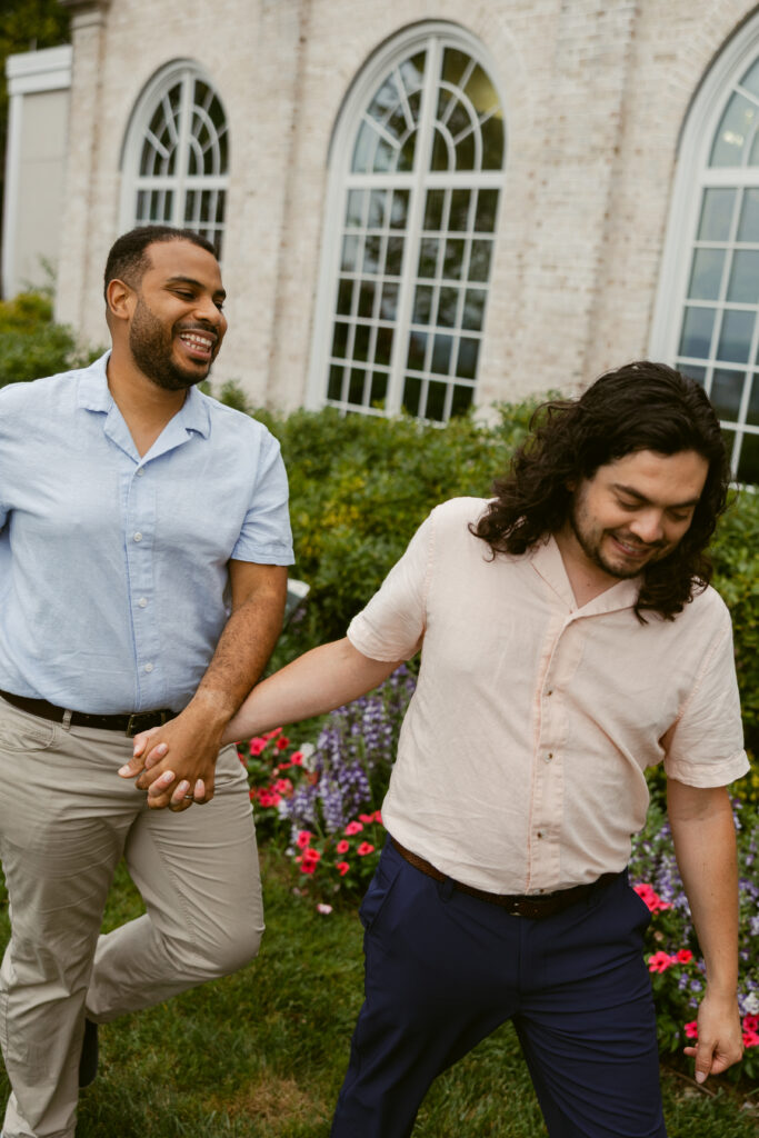 A couple walks holding hands past the arched windows and green bushes at Hershey Gardens